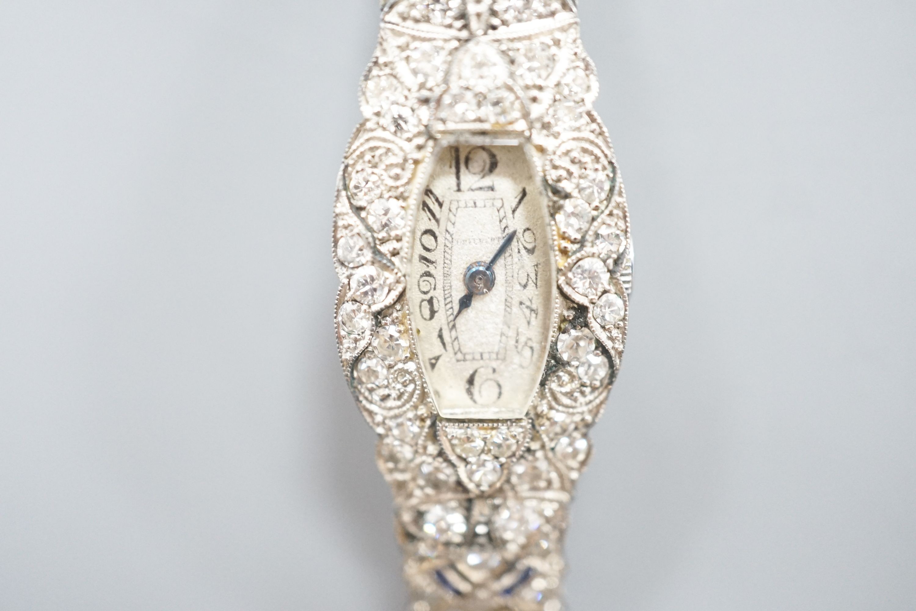 A lady's mid 20th century engraved white metal, diamond and sapphire set cocktail watch, case diameter 17mm, gross weight 18.3 grams, on a later? twin strand fabric strap.